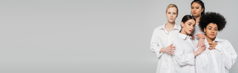 young multiethnic women in white shirts touching each other while posing isolated on grey, banner.