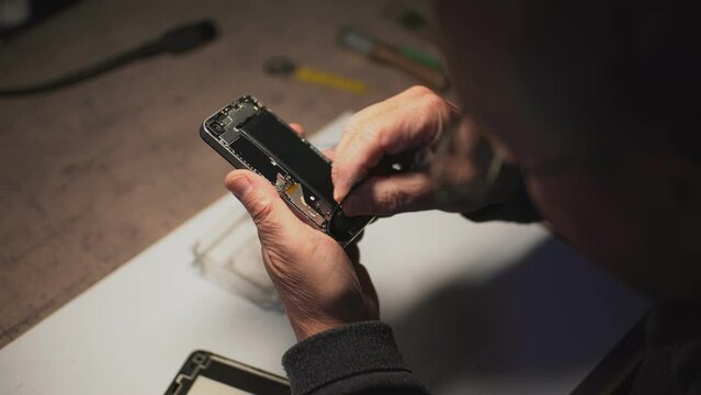 an adult man in the workshop repairs a smartphone. the master uses a magnifying loupe. battery replacement. close-up. High-quality shooting in 4k format