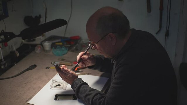 an adult man in the workshop repairs a smartphone. battery replacement. looking for smartphone malfunction.close-up. High-quality shooting in 4k format