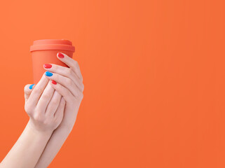 Close-up of a thermo-cup held in female hands with bright manicure. Cafe branding of takeaway coffee. Ecology concept of zero waste lifestyle showing the reusable hot beverage container.