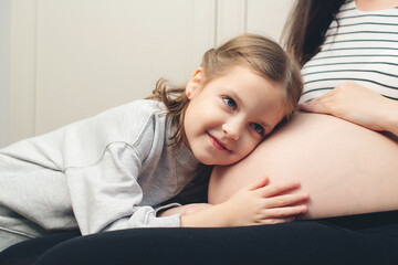 Happy little girl touching her pregnant mom tummy. Pregnant mother and daughter spending time together at home.