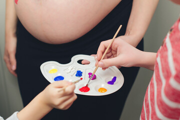 Baby birth expecting time and belly painting. Happy children and pregnant mom having fun together at home.