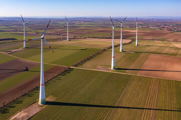 Obraz premium A wind farm with wind turbines between fields seen from the air from high above