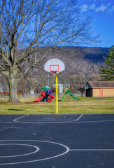 The basketball court and playground are empty on this beautiful but still very cold Spring Day.  Blue skies and white clouds on a chilly day in Kirkwood in Upstate NY.  Nobody around playing today!