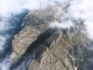 Aerial drone photo of green forest covered mountains, flying through light wispy clouds.Calp, Alicante, Spain