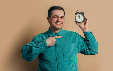 Stylish caucasian man in green shirt with vintage alarm clock on brown background