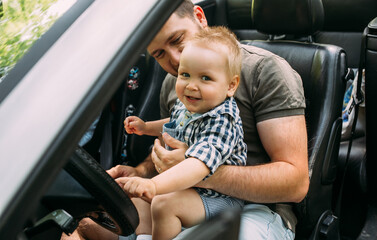 Dad shows his little son how to drive car while sitting behind wheel