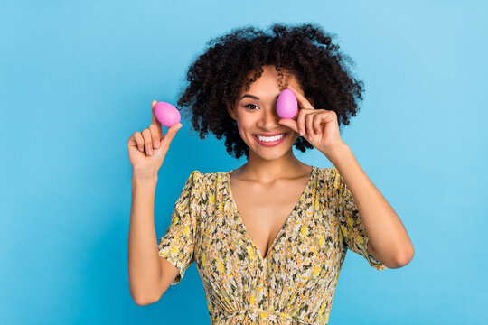 Photo of shiny pretty woman wear print dress rising pink easter eggs cover eye isolated blue color background
