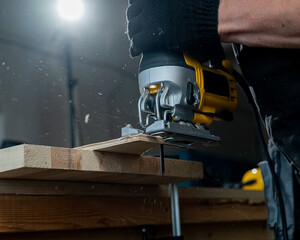 Close-up of a man cutting a wooden plank with an electric jigsaw in a workshop.