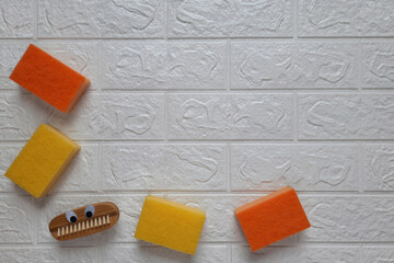 Fun brush and kitchen sponges for cleaning. Copy space. Fun cleaning concept. Scrubbing brush with eyes and dishwashing sponge on brick wall background. Flat lay. Household duties for children.