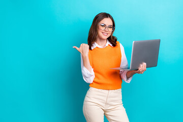 Photo of young positive satisfied businesswoman wear office uniform eyewear hold laptop direct finger empty space isolated on cyan color background