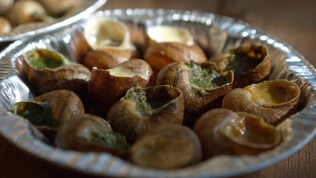 Extreme close-up plate with cooked escargot in sunlight outdoors. Closeup delicious exotic food on wooden table