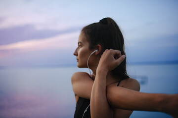 Young sportive girl stretching in the morning and listening music, outdoor near the lake.