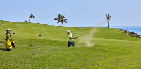 The golf player hits the ball from the bunker with a golf club, on a sunny day in summer.