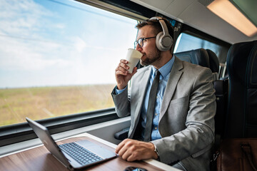 Handsome businessman is having a good time while traveling by high-speed train. He is using laptop...
