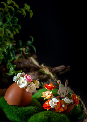 Easter still life with eggs and flowers on green grass, black background
