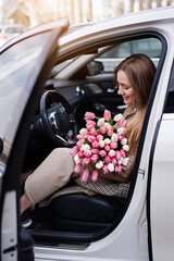 Beautiful girl with tulip flowers in her hands in the car 