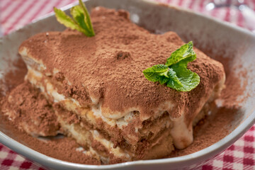 Tiramisu cake with fresh mint, close-up in a deep plate