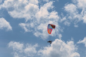 Colorful paraglider or paramotor flying in the blue sky with white clouds.