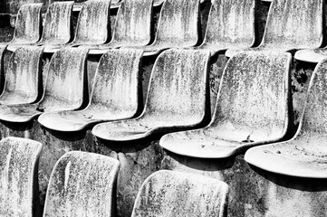 Rows of old chairs dilapidated by time, rain and sunlight. Chairs in a sports facility with...