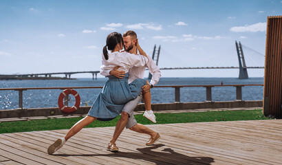 Professional dancers dancing at embankment with view on bay and bridge. Hispanic couple enjoying vacation at seashore. Beardy man dancing with brunette girl. Newlyweds on honeymoon.