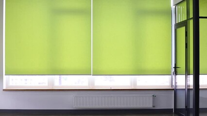 Video of roller blinds close-up on the window in the interior. Roller shades opening up on big windows. Electric curtains for office. Green color, monochrome material. Window coverings.