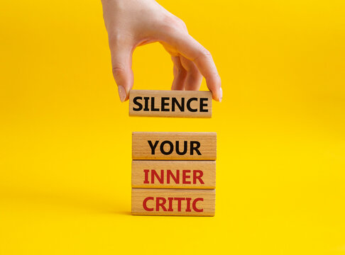 Silence your inner critic symbol. Wooden blocks with words Silence your inner critic. Beautiful yellow background. Businessman hand. Business and Silence your inner critic concept. Copy space.