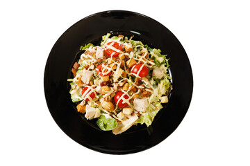 Caesar salad with vegetables, chicken and croutons on a black plate