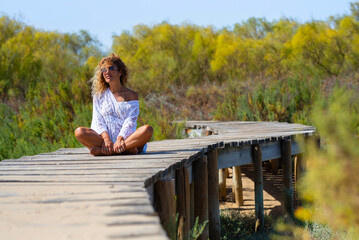 Reborn and freedom lifestyle people meditating and enjoying nature sitting outdoors on a wooden pier in summer. Holiday vacation and travel. Zenlife daydreamer young adult female people outside