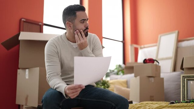 Young hispanic man sitting on sofa reading document at new home