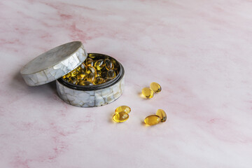 A mother-of-pearl pillbox with pearls of nutritional supplements on a pink marble background