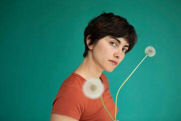 Woman with short hair holding dandelions against green background
