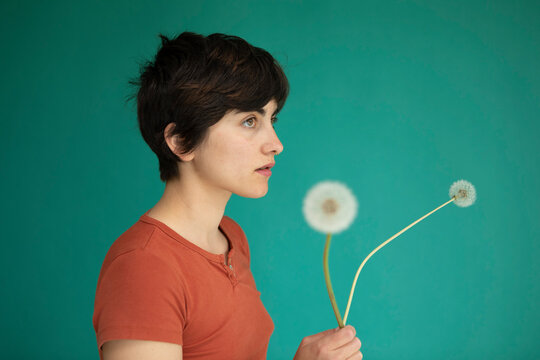 Thoughtful woman holding dandelions against green background
