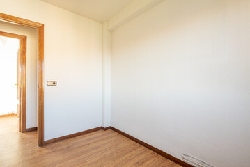 Small empty room with oak flooring, white walls with gotelet and access door to a corridor in front of another similar room