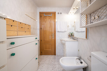 Fototapeta na wymiar Small bathroom with frameless mirror, porcelain sink with marble countertop and mismatched cabinets for drawers and door made of pine wood