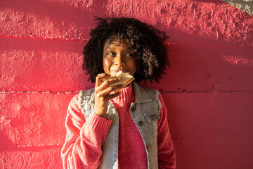 Smiling young woman with sandwich standing in front of red wall