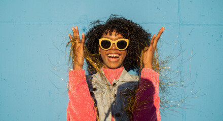 Cheerful woman holding golden party streamers in front of blue wall