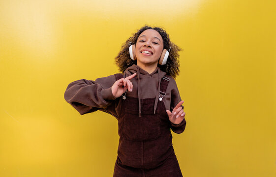 Happy woman with headphones dancing in front of yellow wall