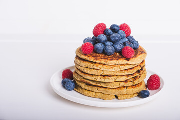 Delicious freshly cooked thick and fluffy gluten free pancakes stacked on white plate, served with fresh berries such as blueberries and raspberries. Healthy food. Place for text.