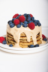 Delicious freshly cooked thick and fluffy gluten free pancakes stacked on white plate, served with cashew cream and fresh berries. Healthy food.