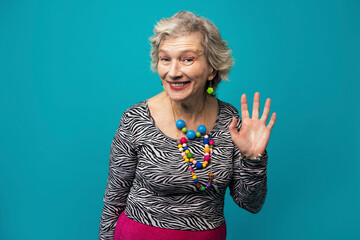Happy senior woman waving against turquoise background