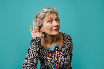 Woman cupping ear to listen against turquoise background