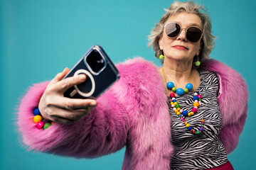 Smiling senior vlogger talking selfie using smart phone against turquoise background
