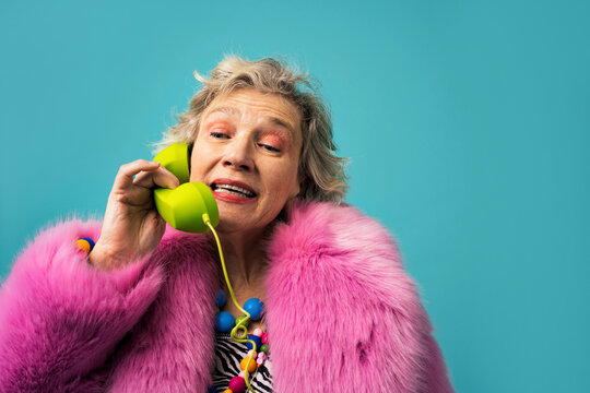 Woman wearing fur coat talking on telephone against colored background