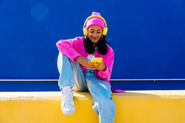 Smiling woman with headphones using smart phone on wall