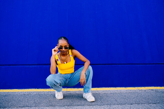 Young woman sitting in squatting position in front of blue wall