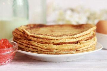 Stack of freshly baked pancakes lie in white plate. Pancake week. Selective focus. Glass bottle with milk, crepes, caviar and egg