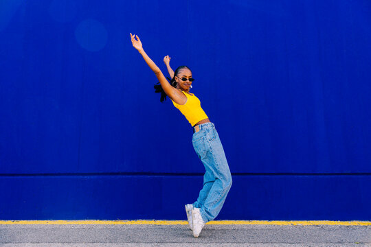 Young woman on tiptoes with arms raised by blue wall