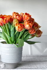 Bouquet of orange tulips in a vase on a blurred light background.