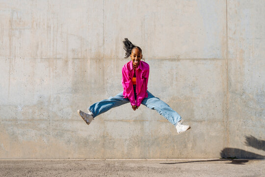 Happy dancer jumping in front of wall on sunny day